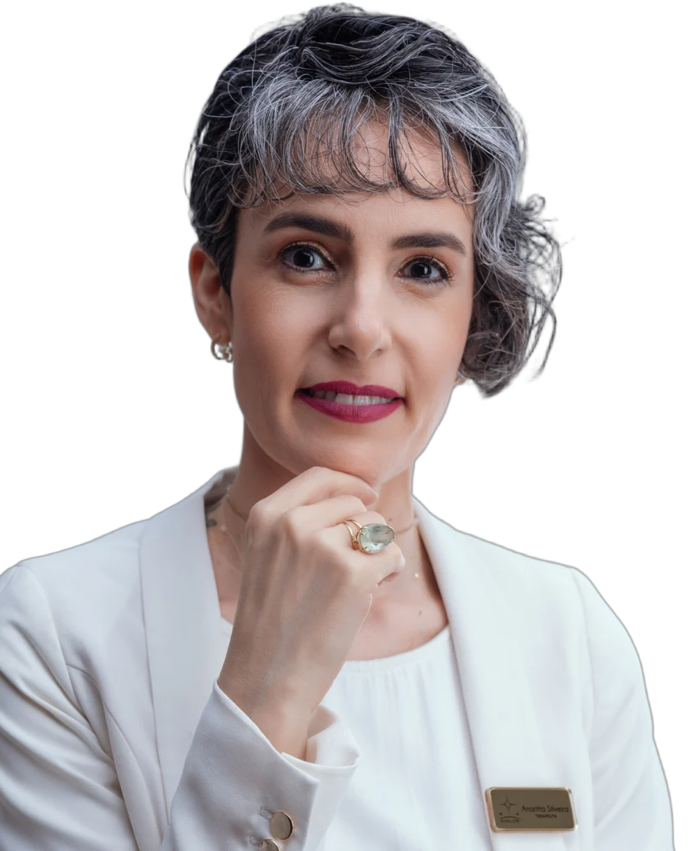 Anaritta Silveira, terapeuta integrativa, de blazer branco, sorrindo com a mão no queixo